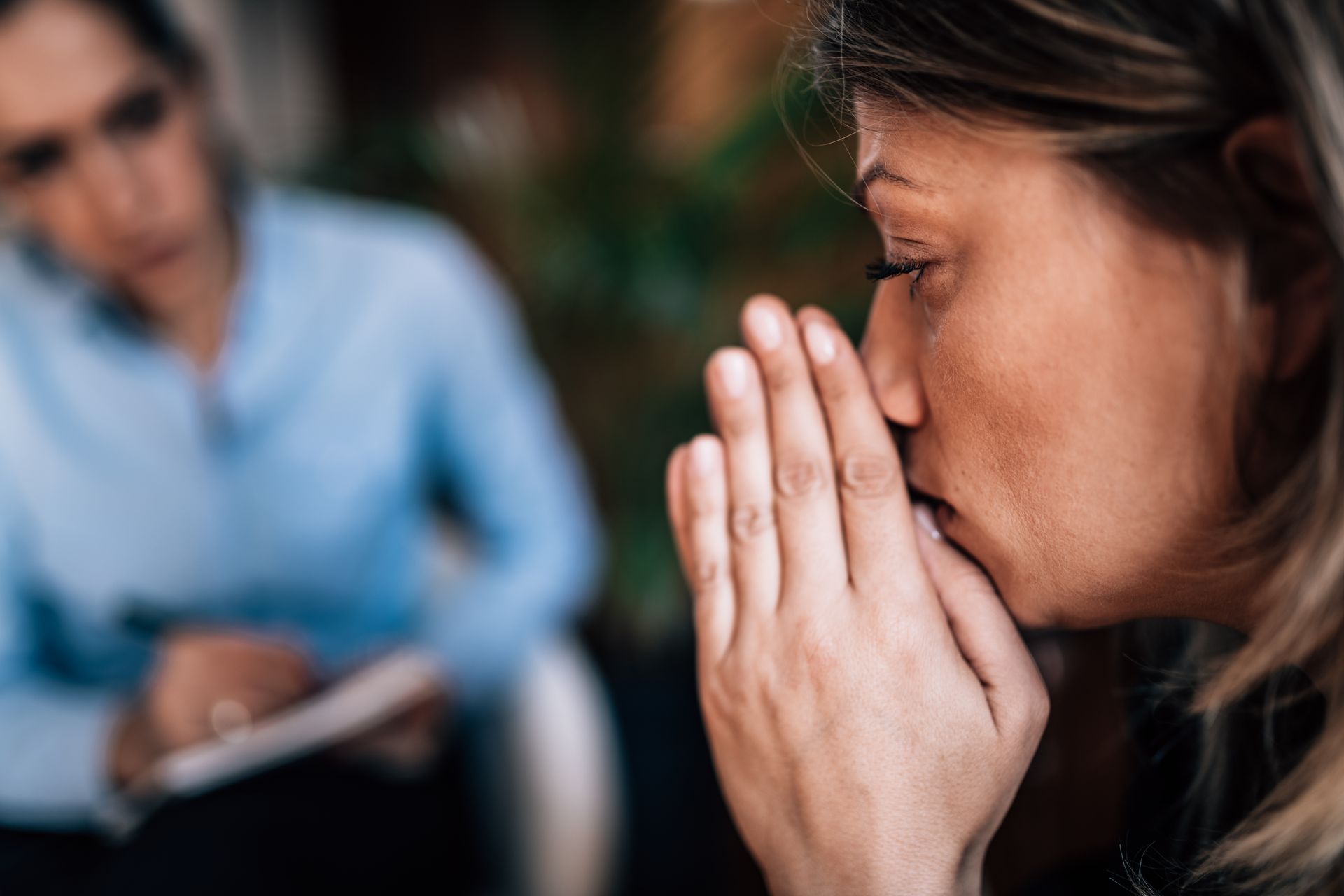 A woman is covering her mouth with her hands while talking to a therapist.