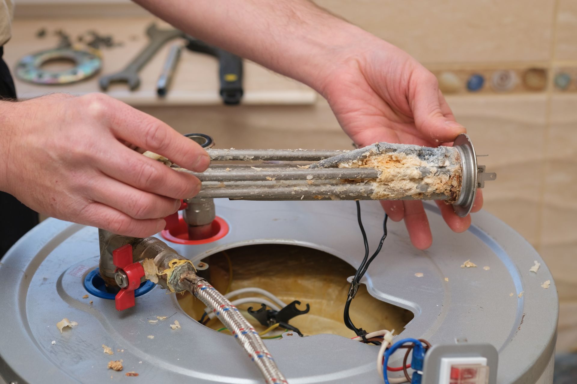 Hands removing a clogged heating element from a water heater tank Hands removing a clogged heating element from a water heater tank