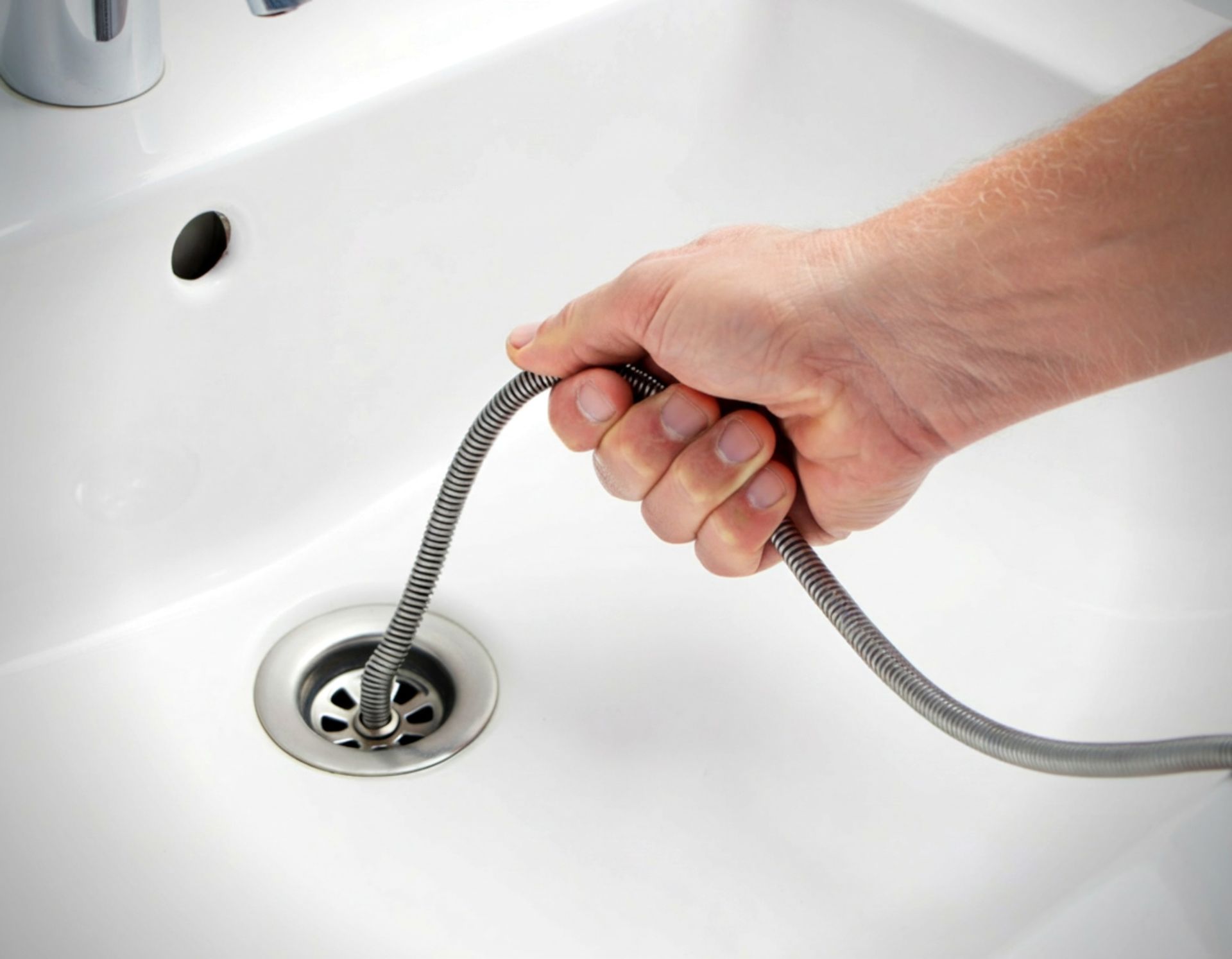 Hand pulling a drain snake from a white sink drain