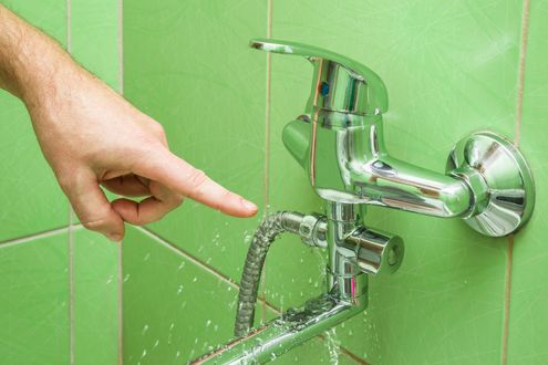 Hand turning on a chrome faucet, with water flowing into a sink against green tiled walls Hand turning on a chrome faucet, with water flowing into a sink against green tiled walls