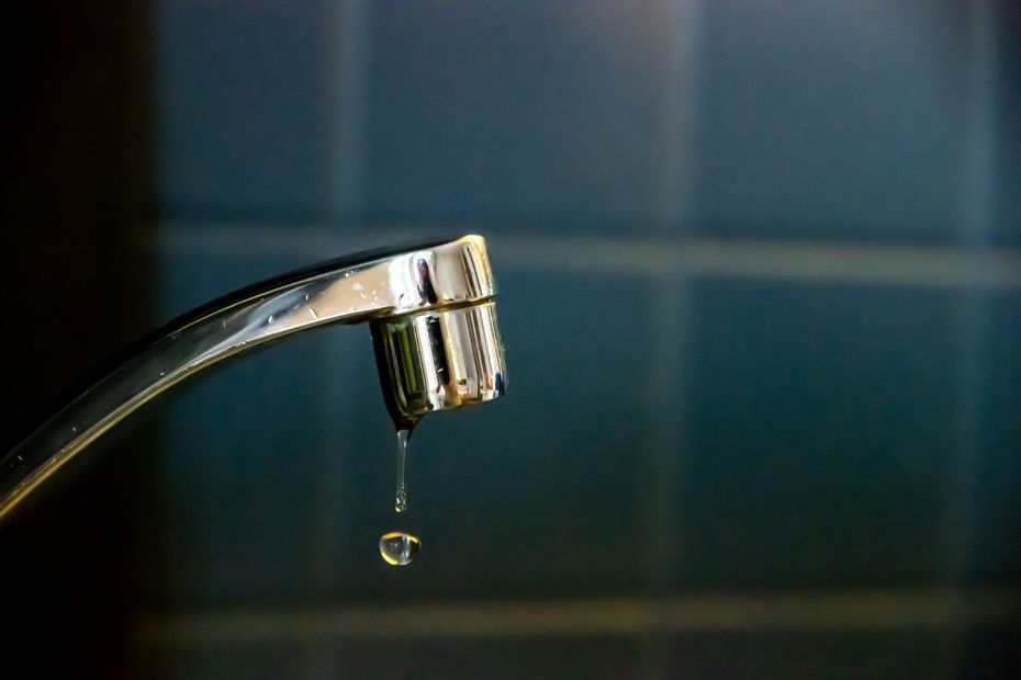 Dripping chrome faucet over a dark tiled sink background Dripping chrome faucet over a dark tiled sink background