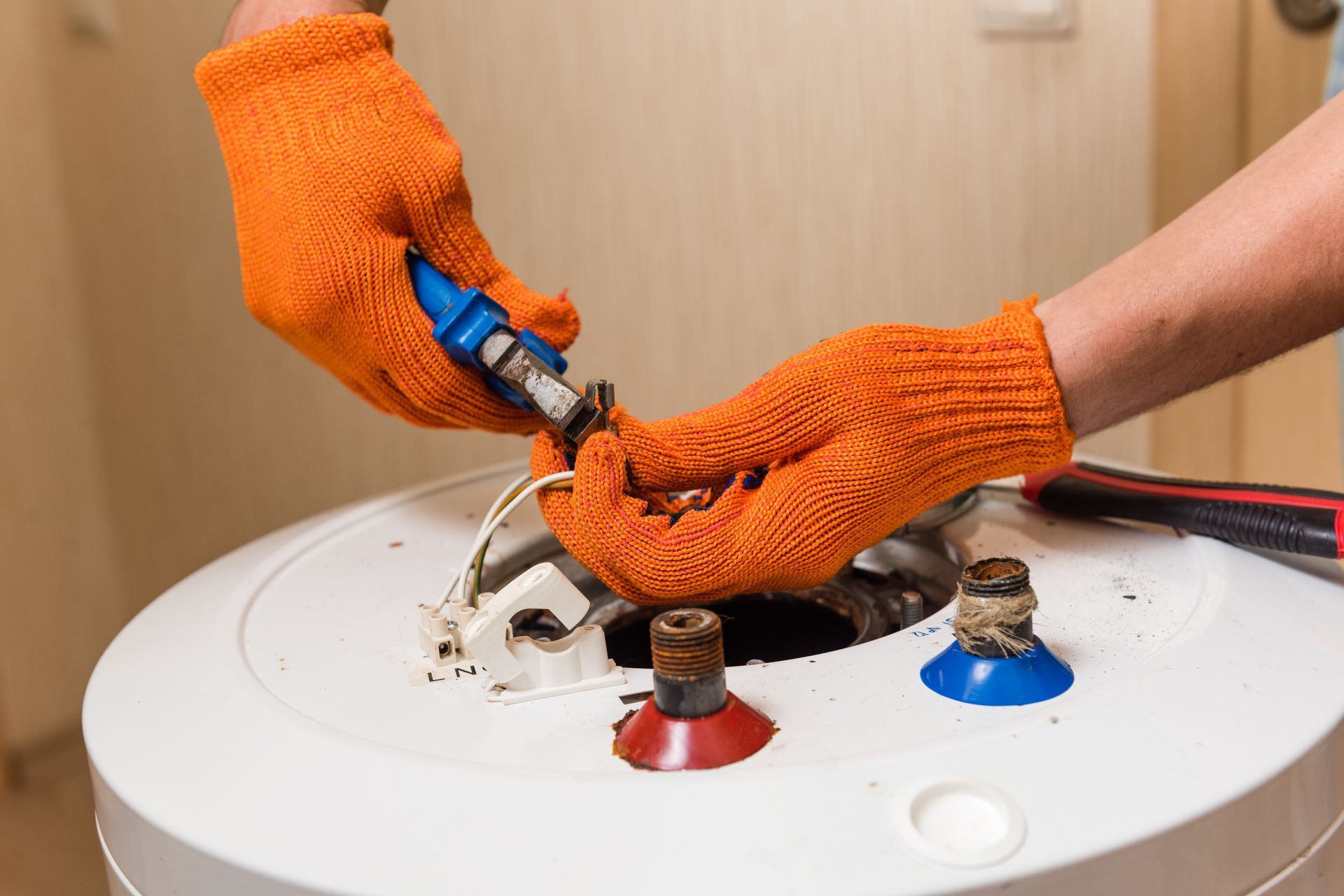 Gloved hands using a wrench to connect hoses on top of a white water heater tank Gloved hands using a wrench to connect hoses on top of a white water heater tank