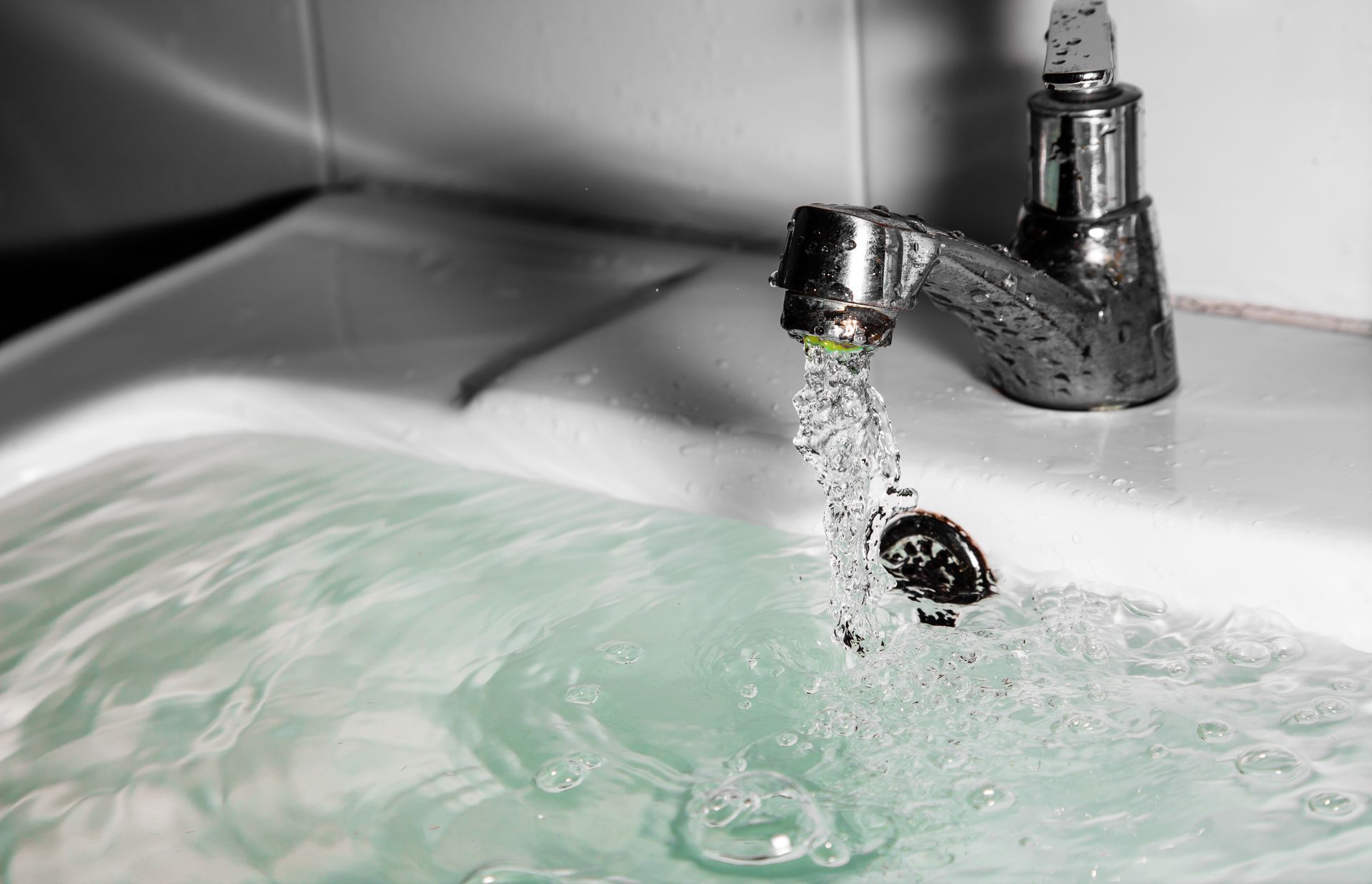 Water running from a faucet into a sink, filling with pale green-tinted water. Water running from a faucet into a sink, filling with pale green-tinted water.