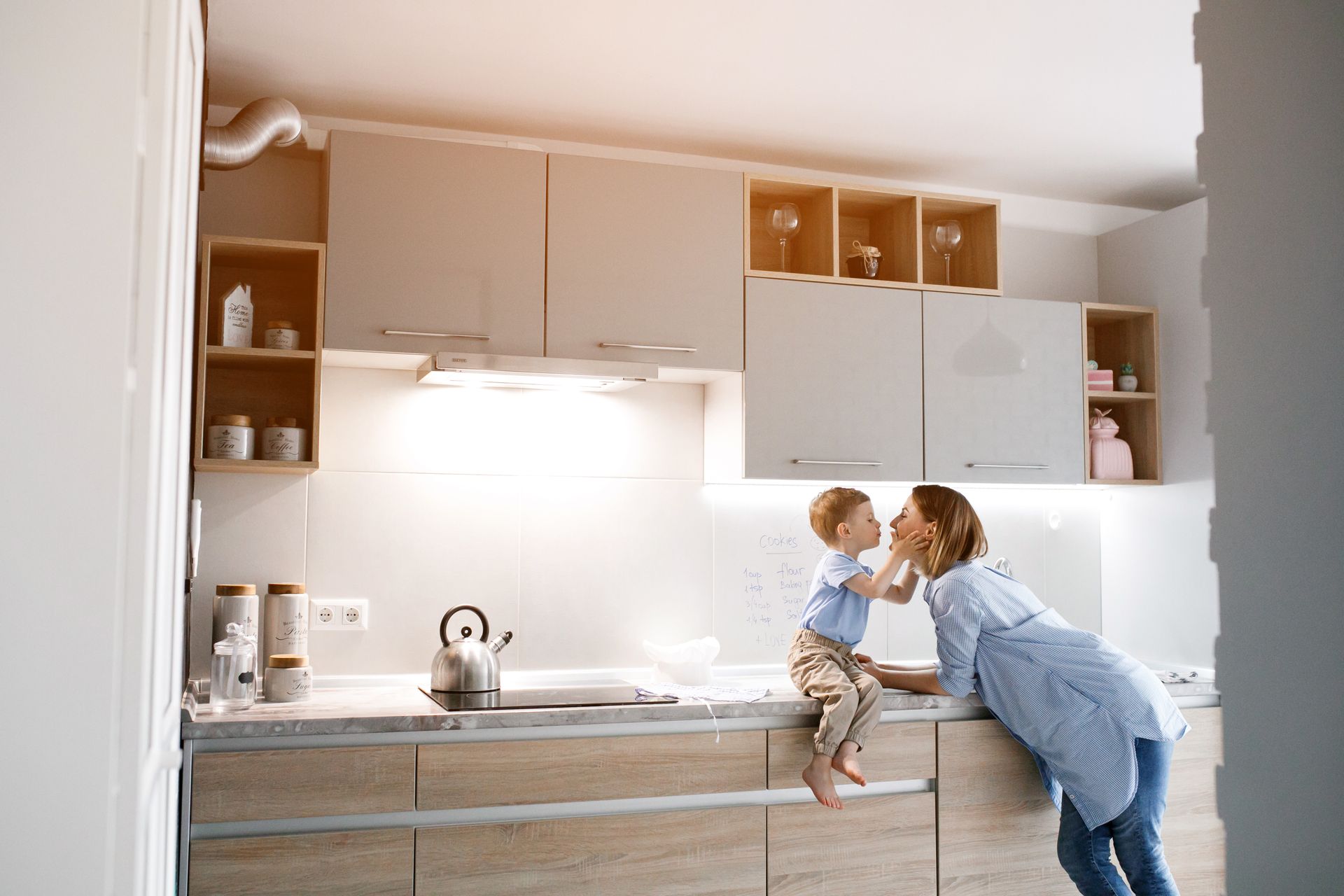 Adult helping a child in a bright modern kitchen, reaching up near the counter. Adult helping a child in a bright modern kitchen, reaching up near the counter.