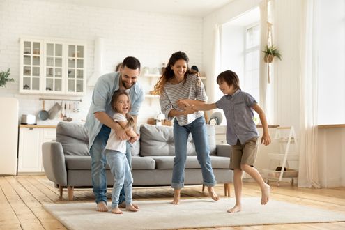 Family standing in a bright living room, smiling and playing together near a sofa Family standing in a bright living room, smiling and playing together near a sofa