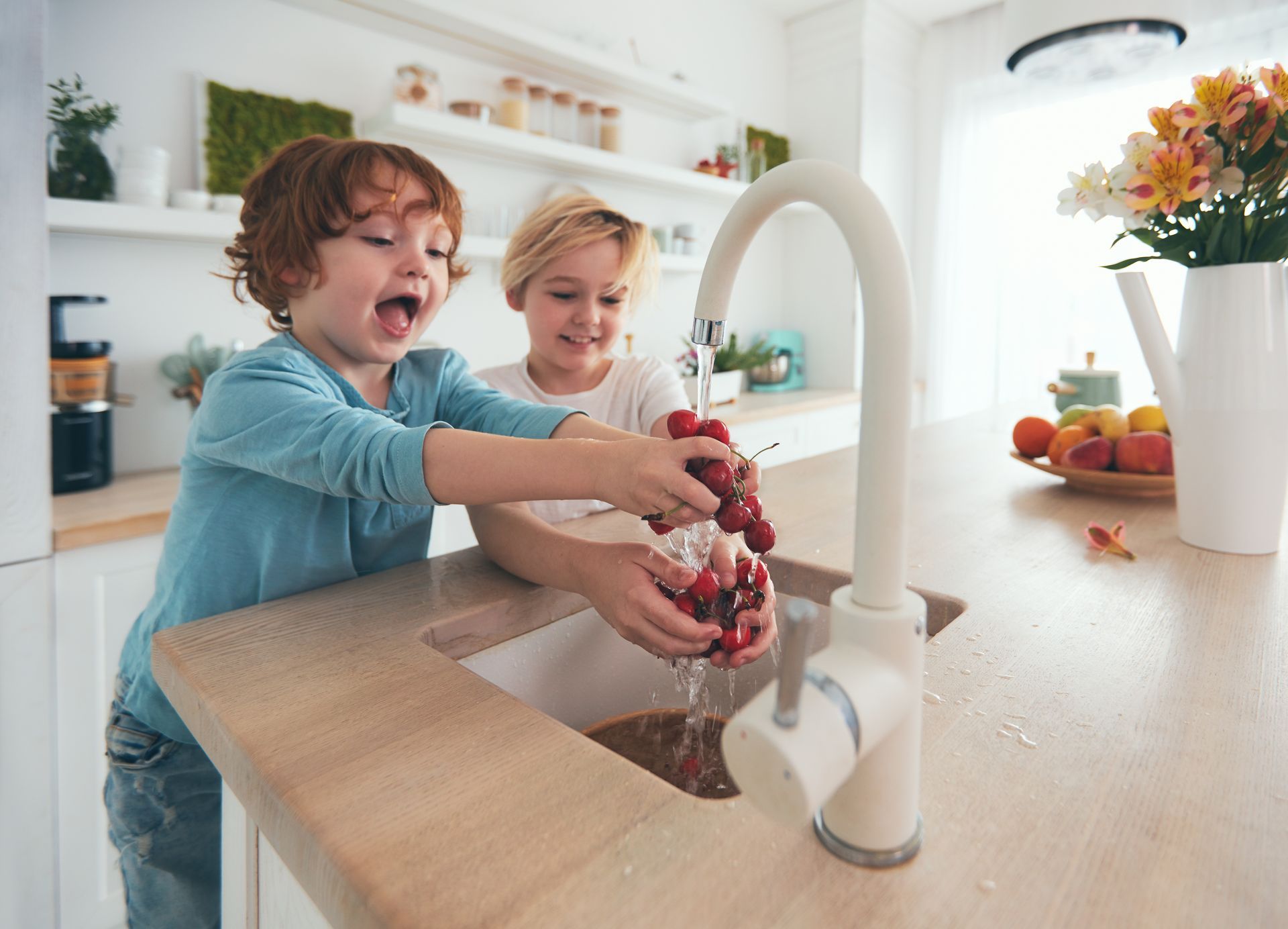Two children washing red berries together at a kitchen sink in a bright home kitchen Two children washing red berries together at a kitchen sink in a bright home kitchen