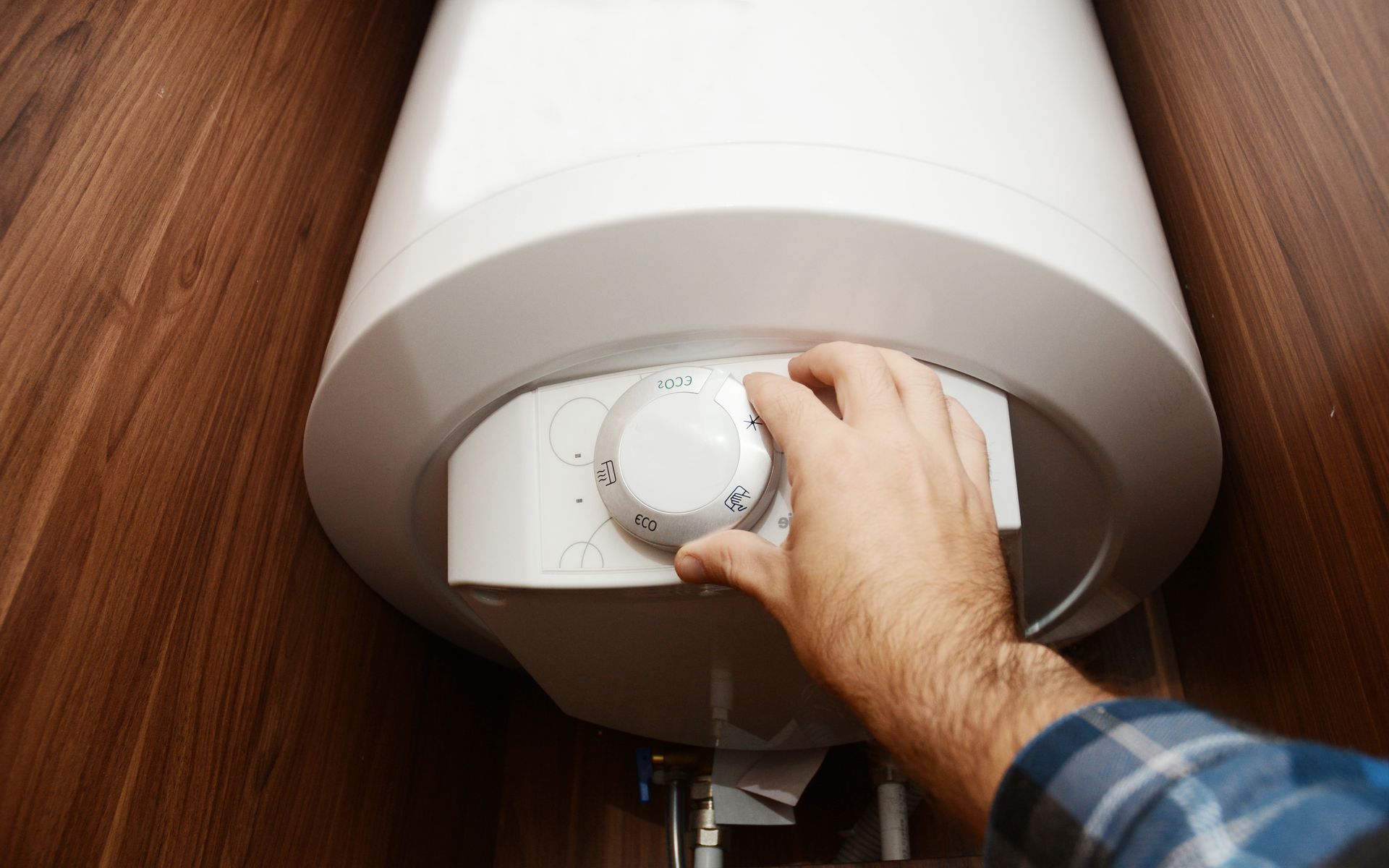 Hand turning the temperature dial on a white wall heater mounted above a wooden floor Hand turning the temperature dial on a white wall heater mounted above a wooden floor