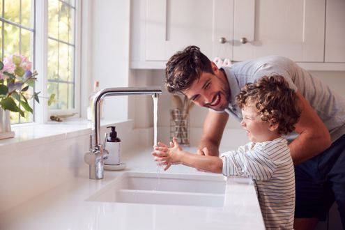 Adult helping child wash hands at a kitchen sink by a bright window Adult helping child wash hands at a kitchen sink by a bright window