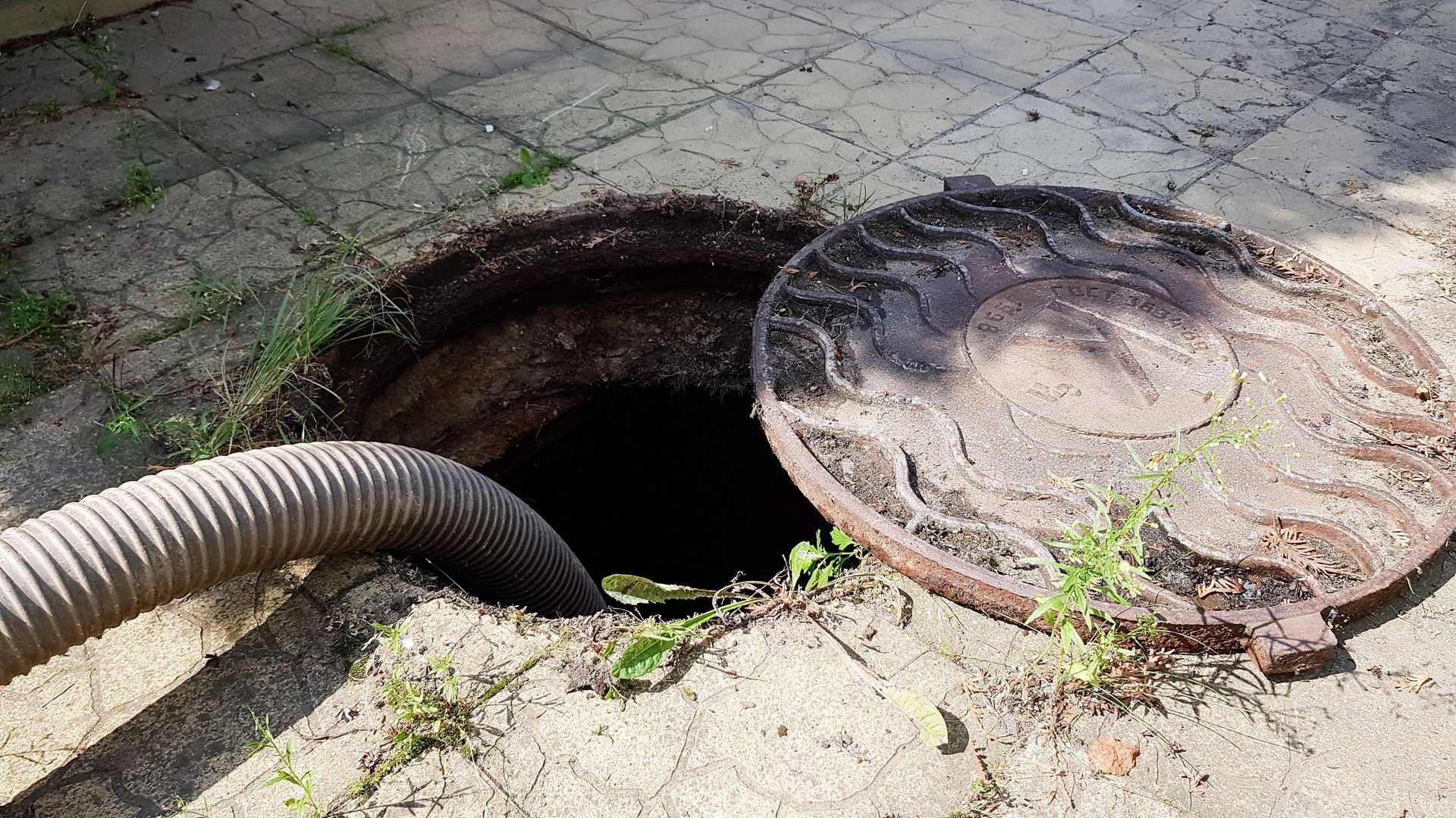 Open manhole with a hose leading into it on a paved surface, cover lying beside the opening Open manhole with a hose leading into it on a paved surface, cover lying beside the opening