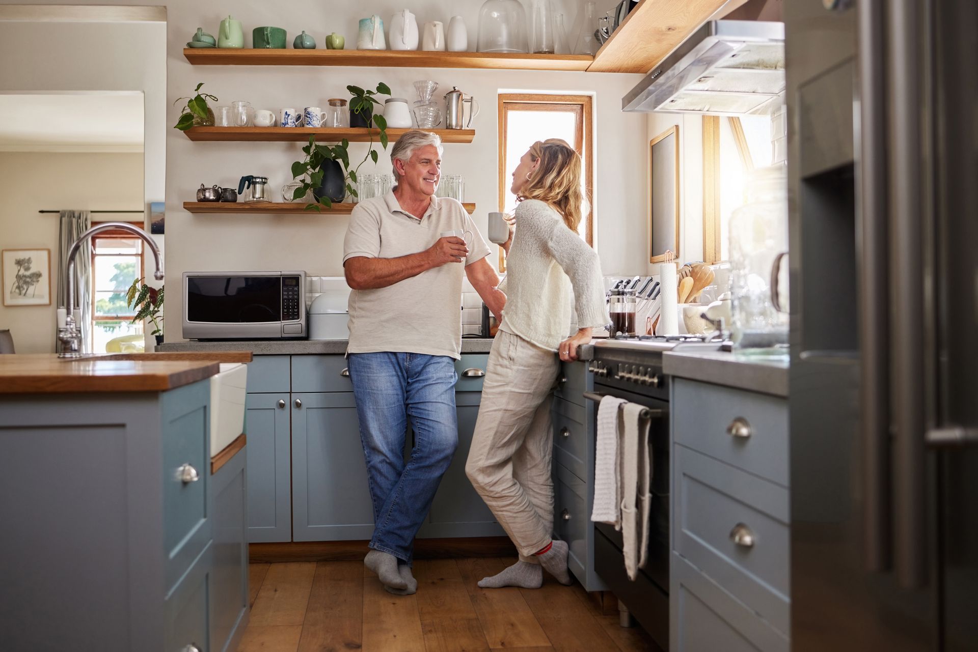 Two people chatting in a bright kitchen with blue cabinets and wooden shelves. Two people chatting in a bright kitchen with blue cabinets and wooden shelves.