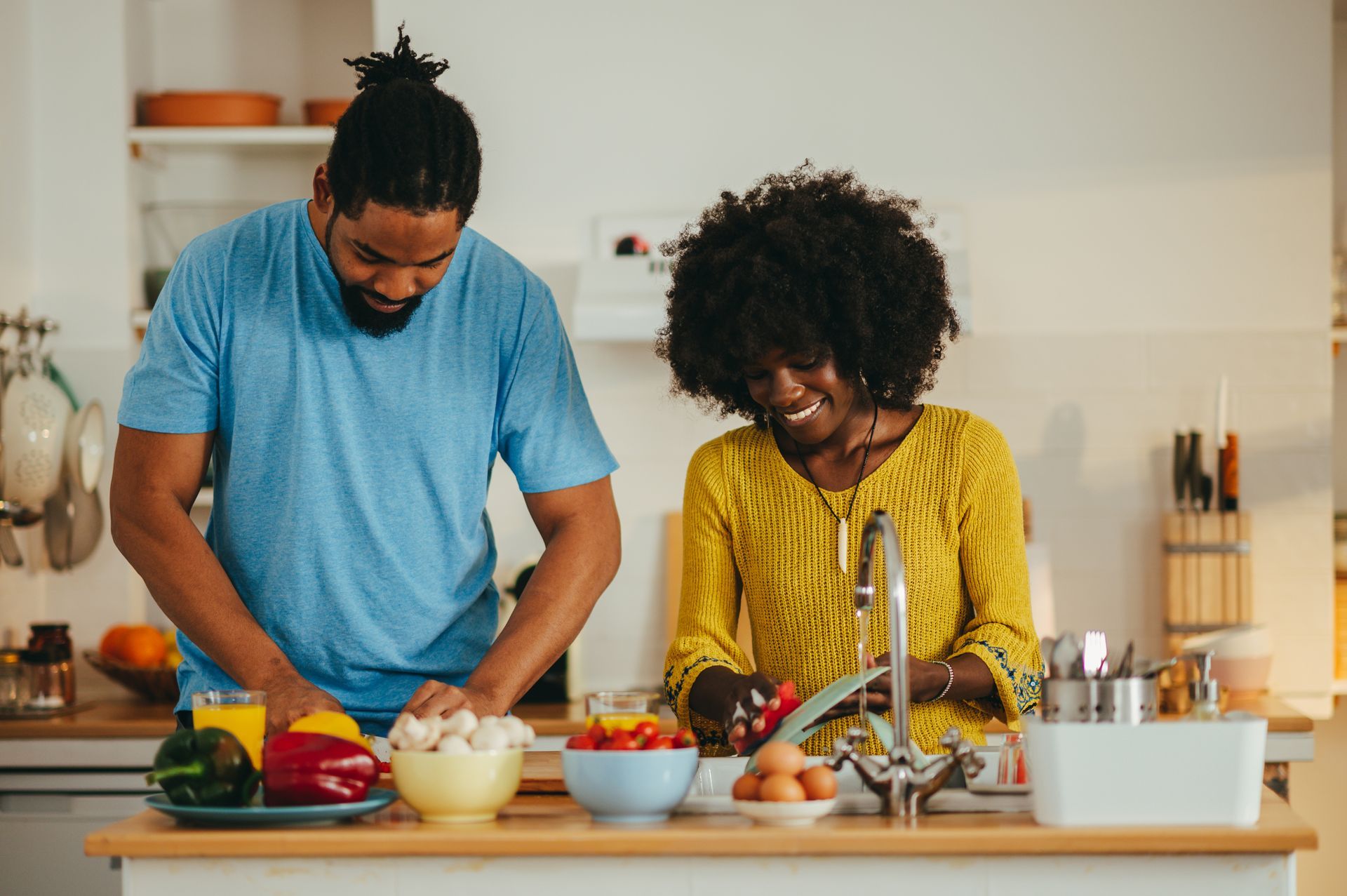 Two people preparing vegetables together in a bright kitchen, with bowls, fruit, and a sink on the counter Two people preparing vegetables together in a bright kitchen, with bowls, fruit, and a sink on the counter