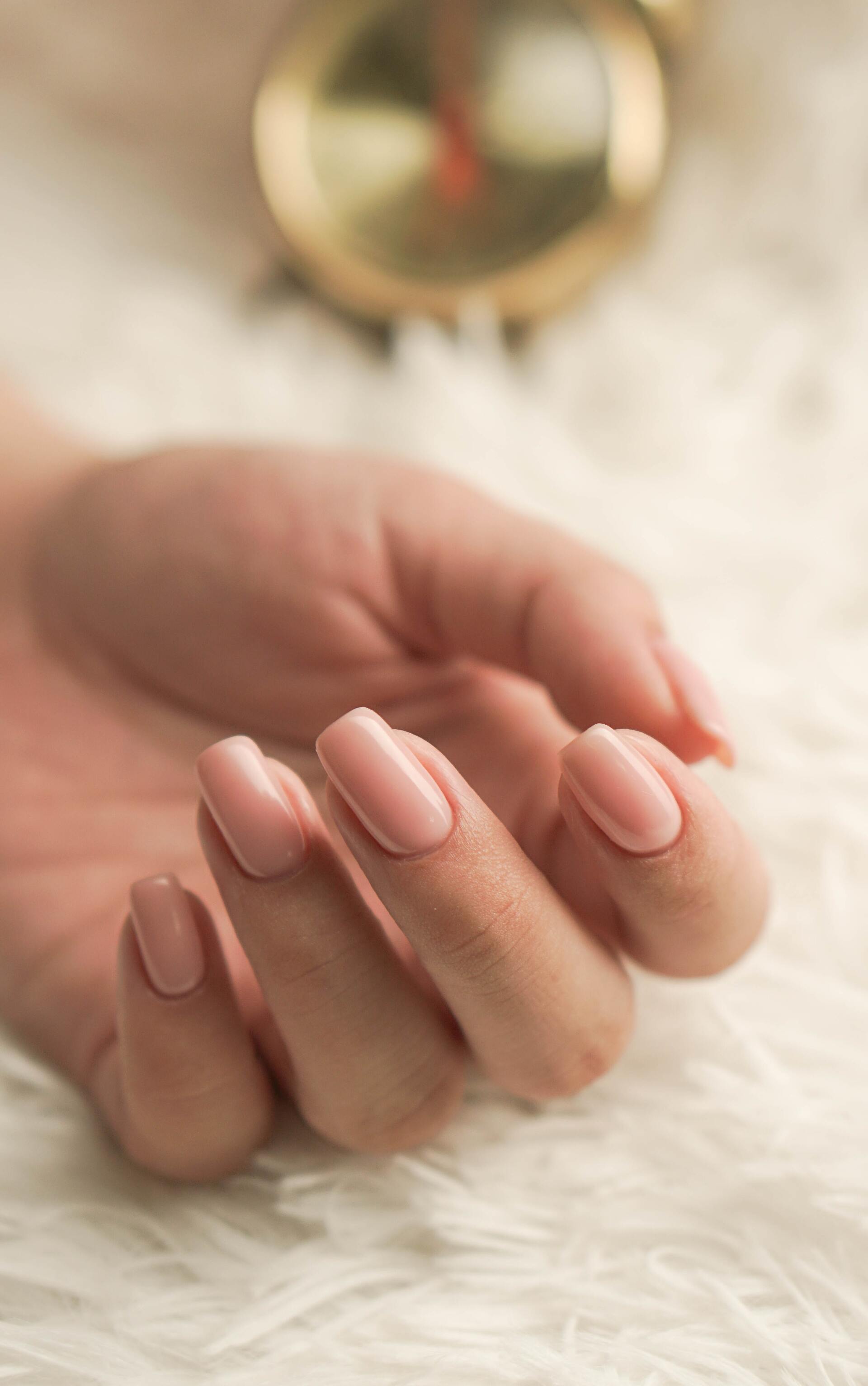 A close up of a woman 's hand with pink nails and a clock in the background.
