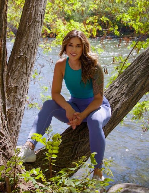 A woman is sitting on a tree branch next to a river.