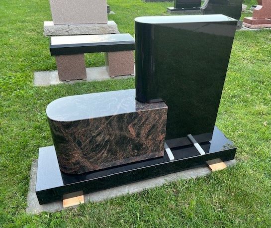 A gravestone with a bench attached to it is sitting in the grass.