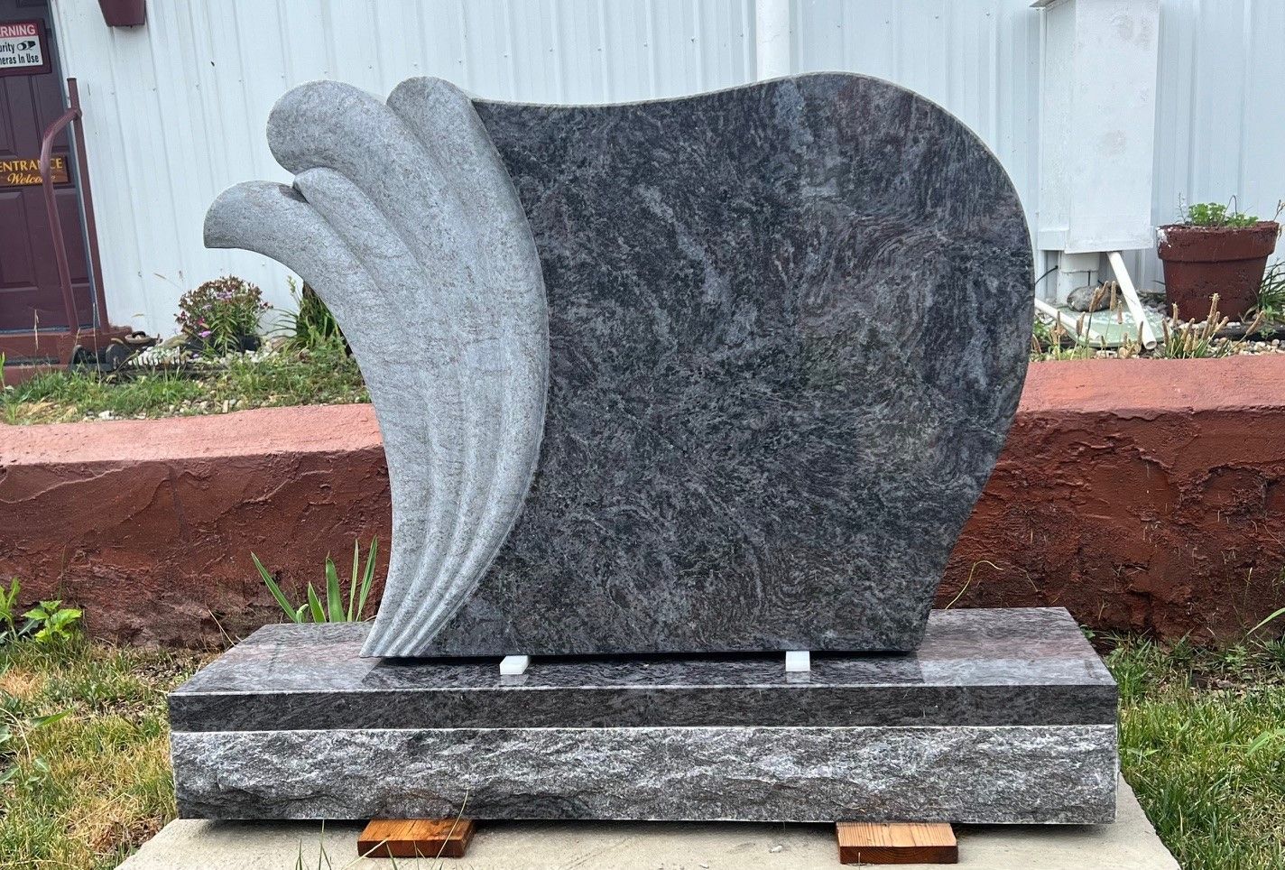 A gravestone with a wing carved into it is sitting on top of a concrete base.