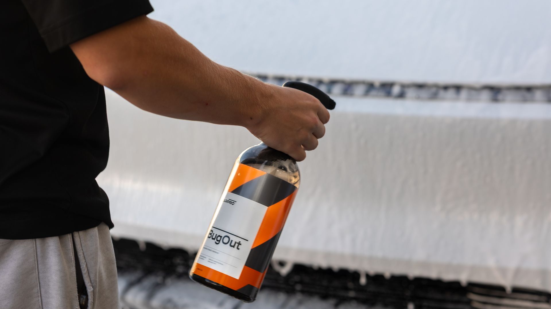 A man is holding a detailing spray bottle, cleaning bugs off his Tesla.