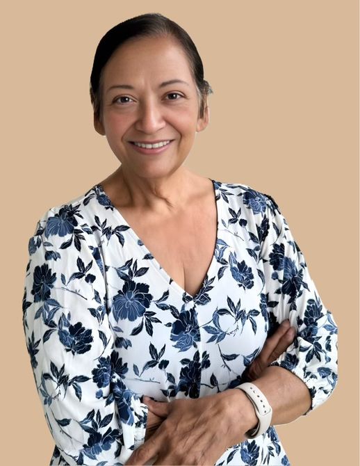 Smiling older woman with dark hair and a floral top, arms crossed. Beige background.