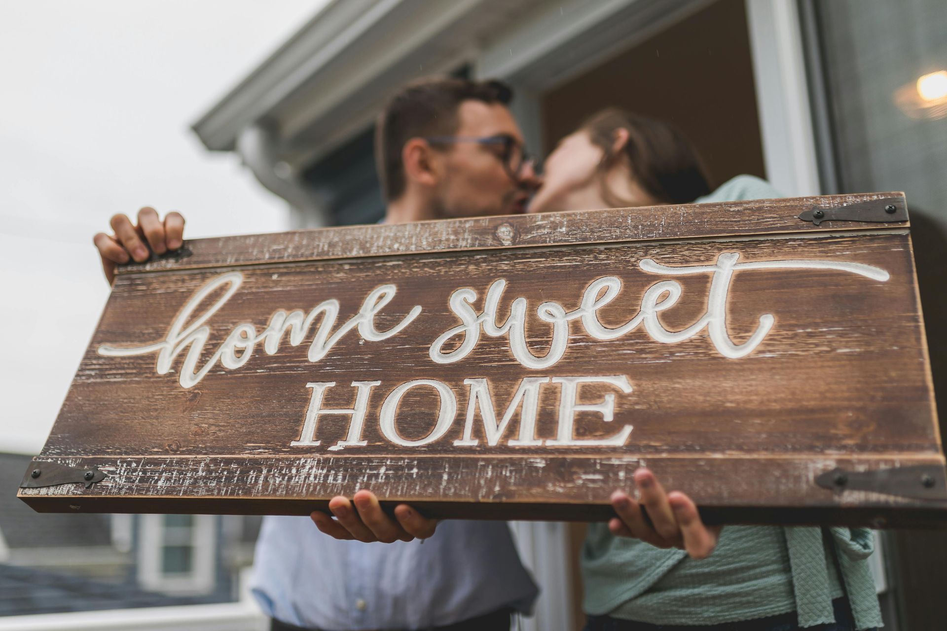 Couple holding a wooden “Home Sweet Home” sign in front of a house