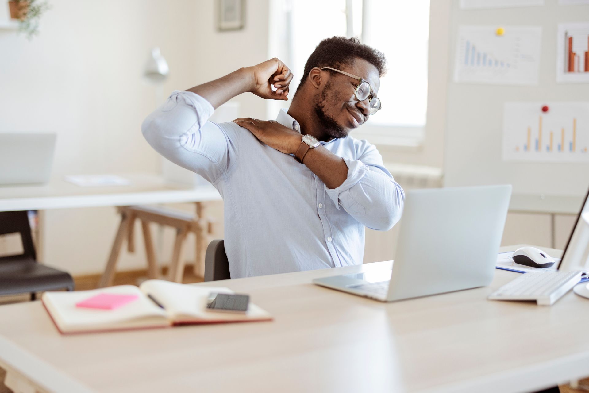 A man is sitting at a desk with a laptop and stretching his arms.