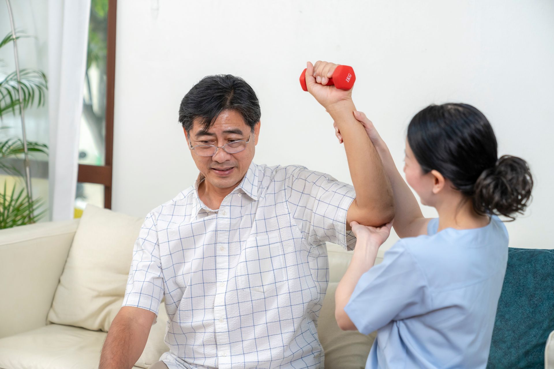 A nurse is helping an elderly man lift a dumbbell.