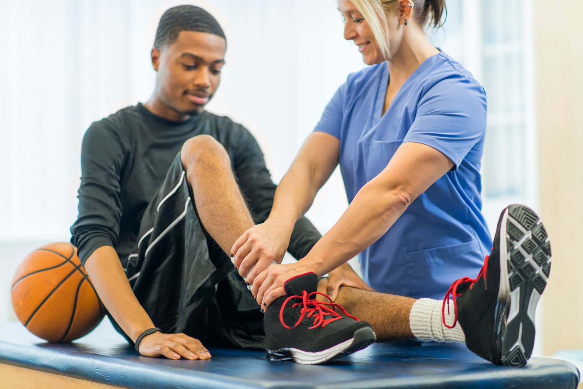 A man is sitting on a table with a nurse helping him with his ankle.