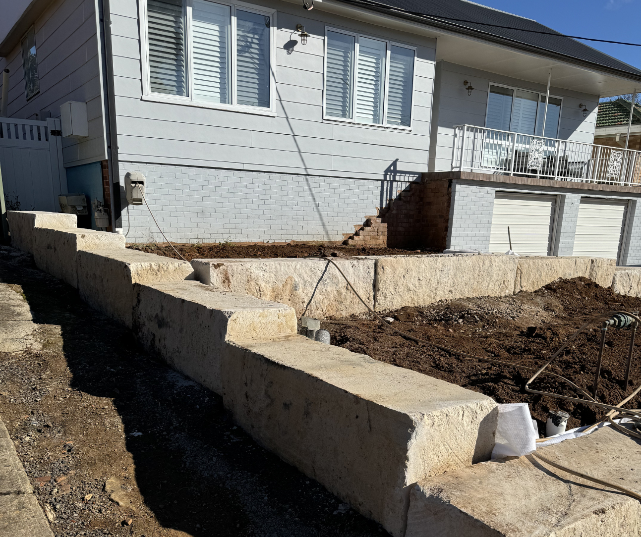Exterior of a house with a raised concrete retaining wall and a dirt yard under construction