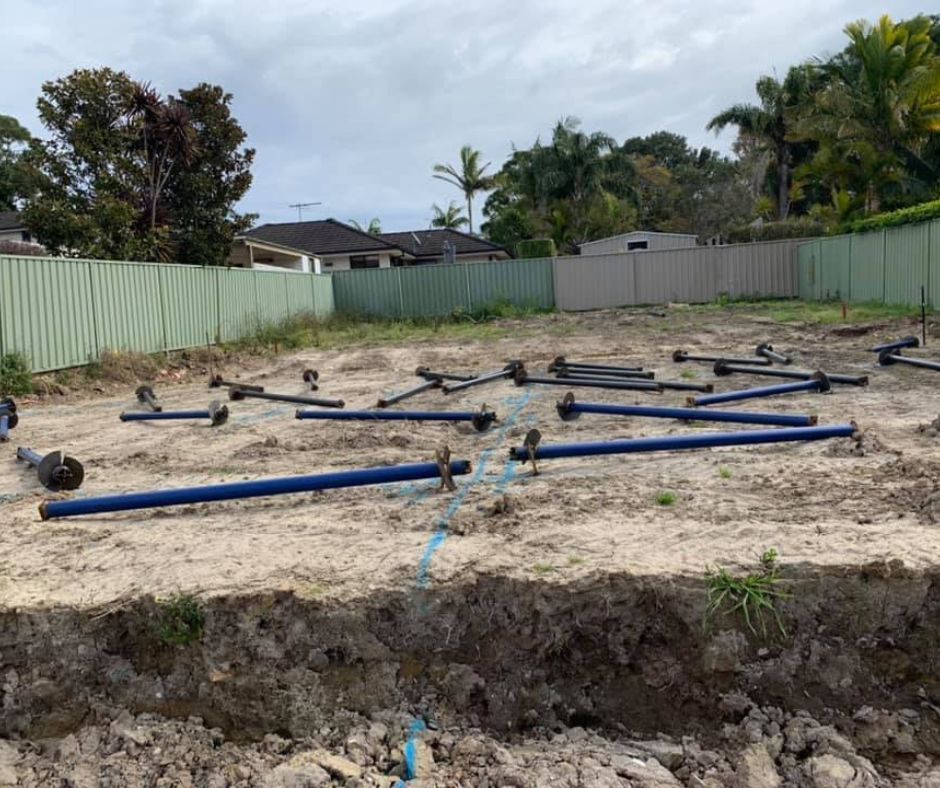 A construction site with blue screw piles lying on marked ground, fenced with houses. 