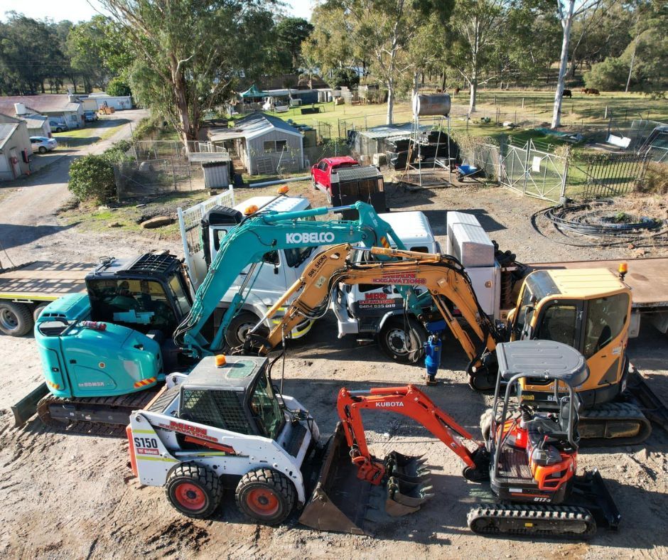 Different excavator types parked on a construction site, including mini, medium, and skid model 