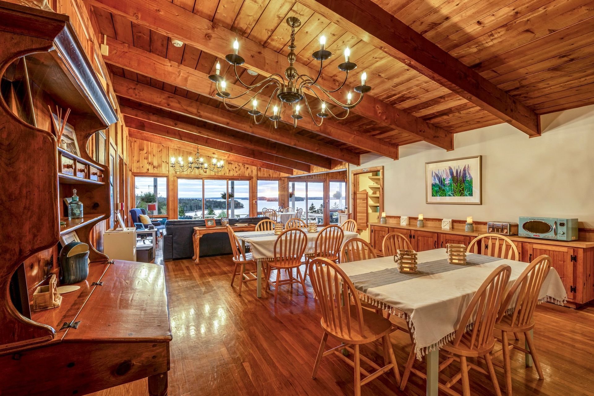 A rustic dining area with wood floors, tables set for meals, and large windows with ocean views.