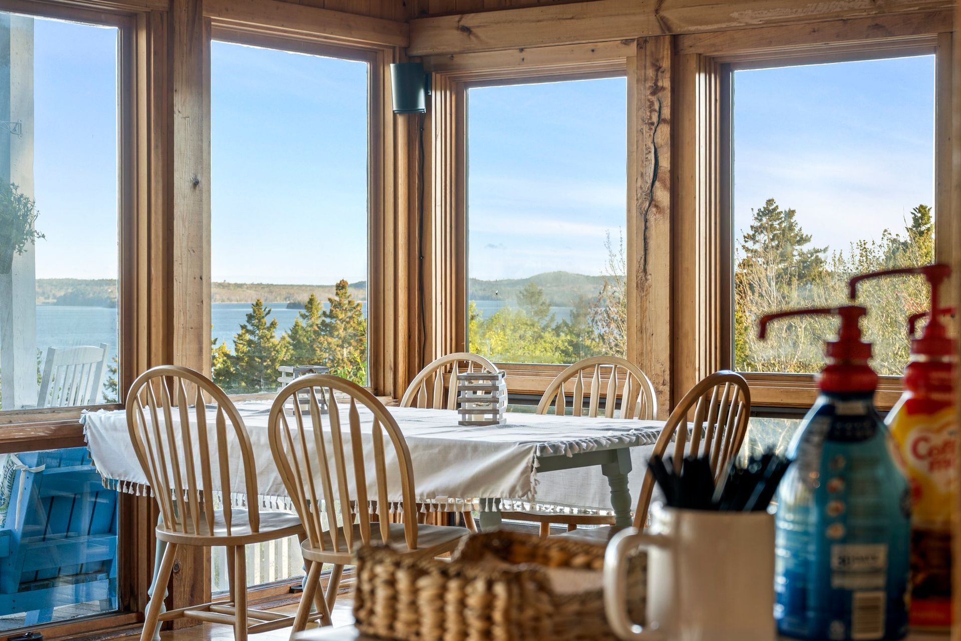 A dining room with a round table set for guests overlooking the ocean. Several wooden chairs surround the table.
