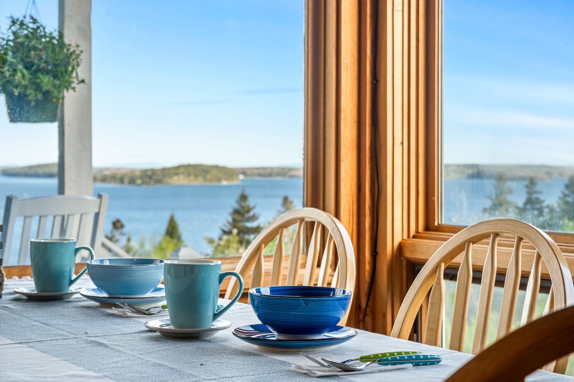 A dining room table with blue bowls and plates and a view of the ocean.
