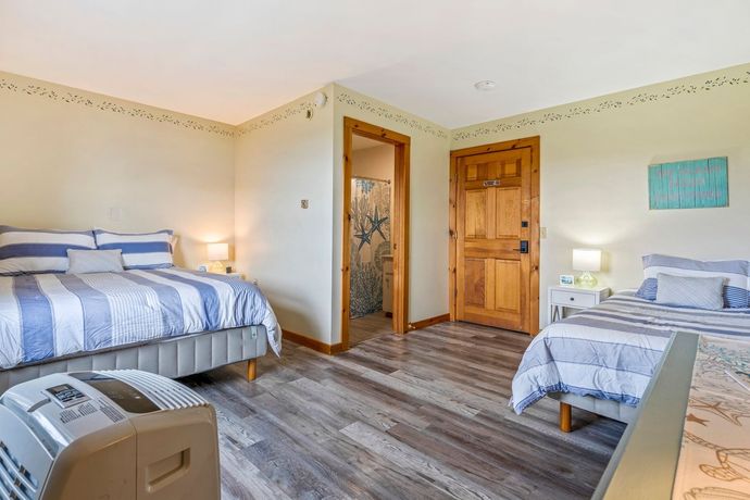 Inn room with two beds. There is a door leading to a bathroom , and the walls are cream colored.