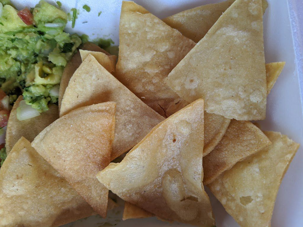 A white plate topped with tortilla chips and guacamole.