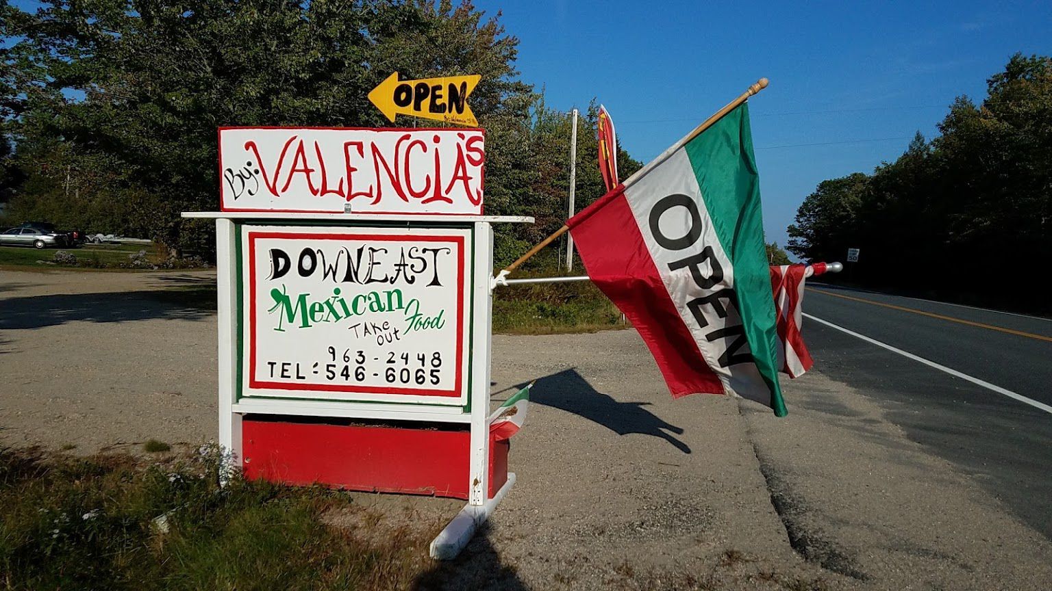 Two flags are flying in front of a sign that says open