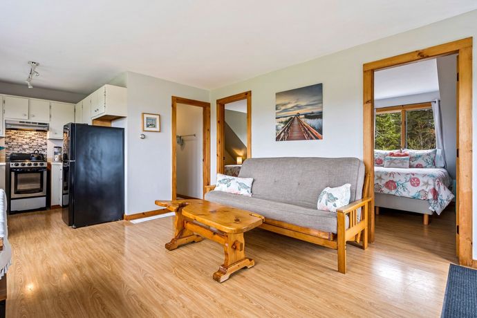 Open-concept living area with a futon, wooden coffee table, and a view into a bedroom with a floral comforter. 