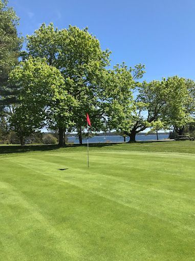 A golf course with trees and a lake in the background.