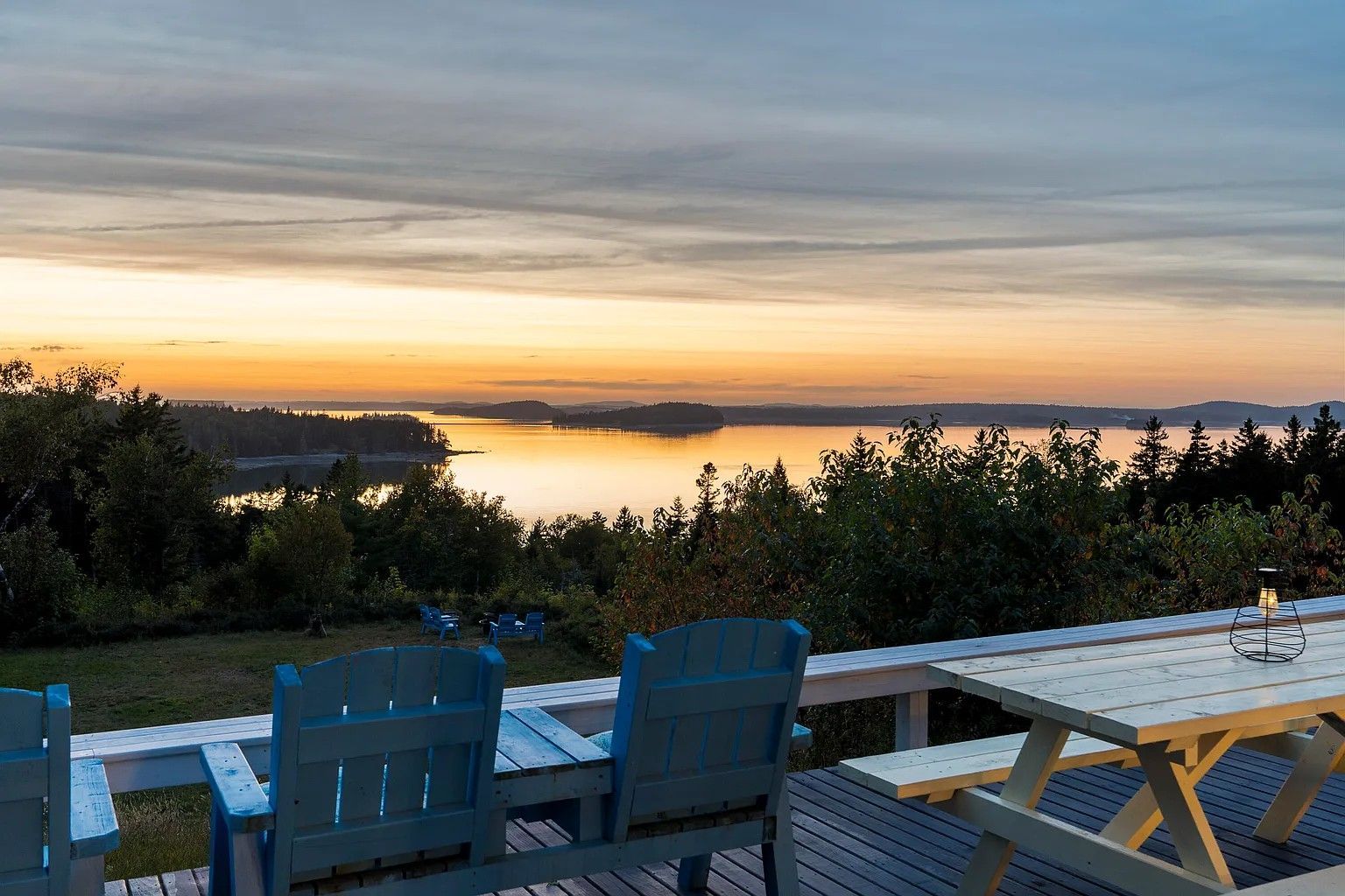 A picnic table and chairs on a deck overlooking a body of water at sunset.