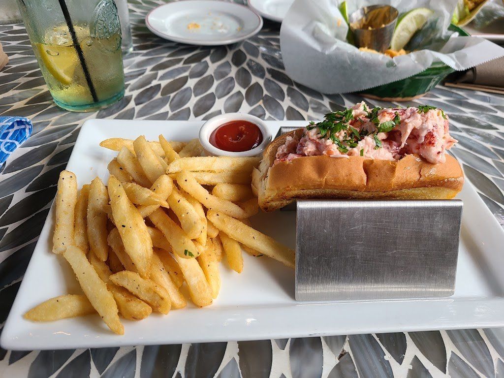 A lobster roll and french fries on a white plate on a table.