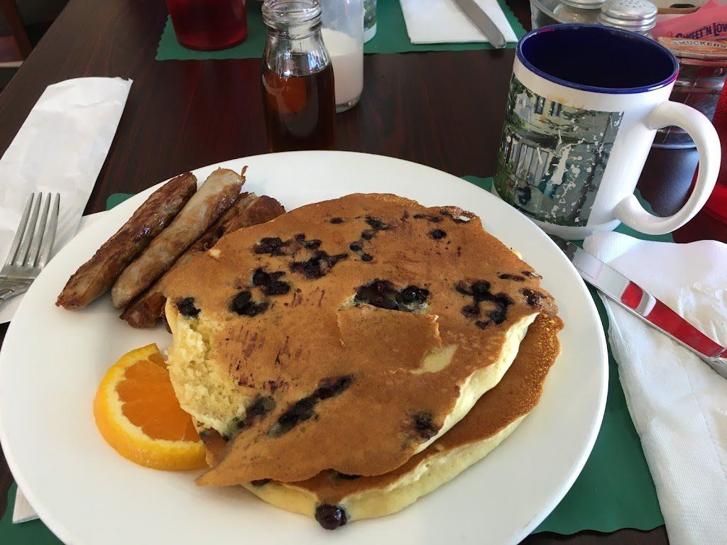 A plate of food with pancakes , sausages , and an orange on a table.