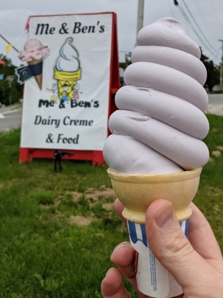 A person is holding an ice cream cone in front of a sign that says me & ben 's dairy creme & feed