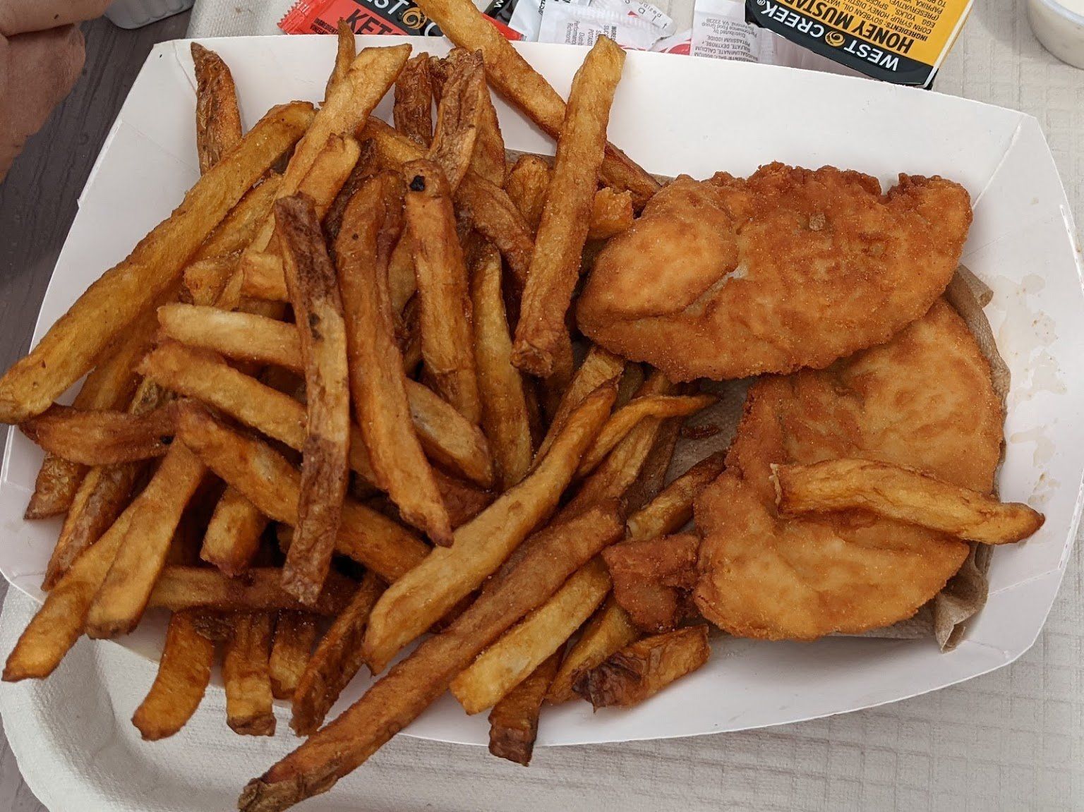 A paper container filled with french fries and fried fish