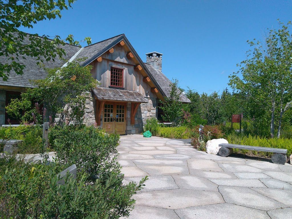 A large stone house with a wooden roof is surrounded by trees and bushes.