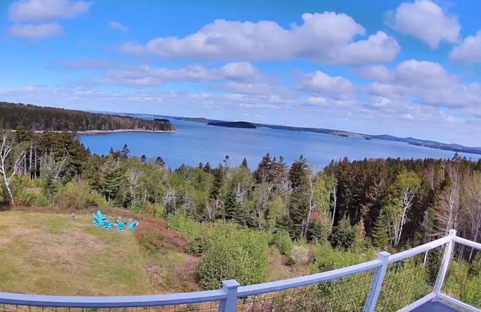 View from a high vantage point overlooking the ocean with islands, forest, and a partly cloudy blue sky.