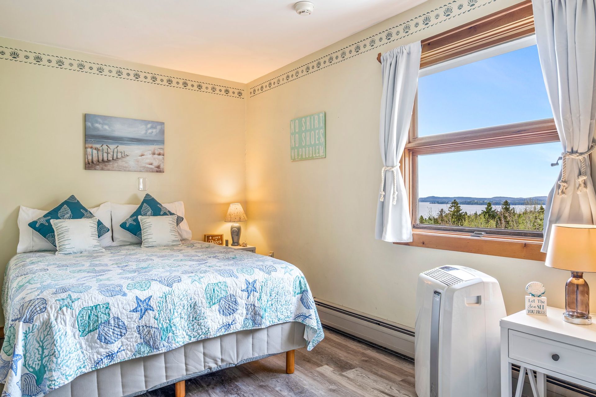 Cozy bedroom with a bed, small table and chairs, and a large window with a view of the ocean.