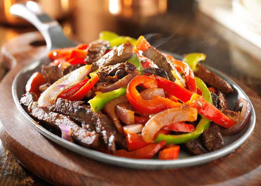 A pan filled with steak and peppers is on a wooden cutting board.