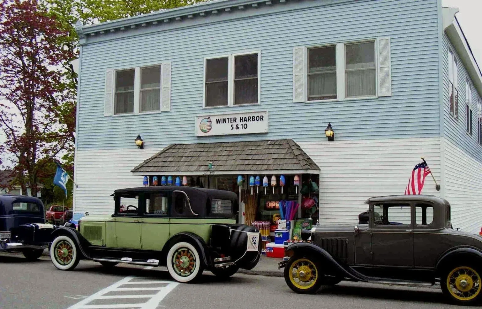 Two old cars are parked in front of a white house inn