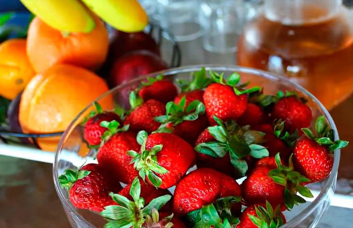 A bowl of strawberries sits on a table next to a bowl of fruit.
