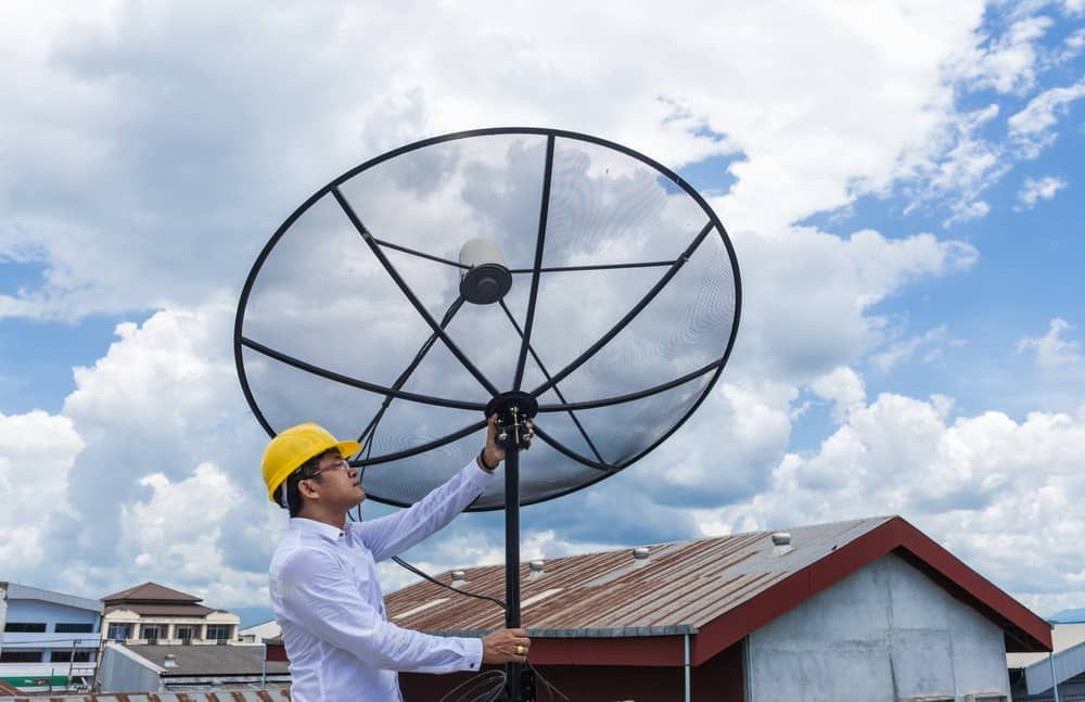A Man Is Standing On Top Of A Roof Holding A Satellite Dish — Coastwide Antennas In Kincumber, NSW