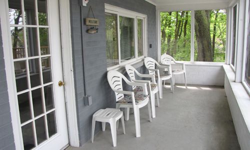 A screened in porch with chairs and a stool