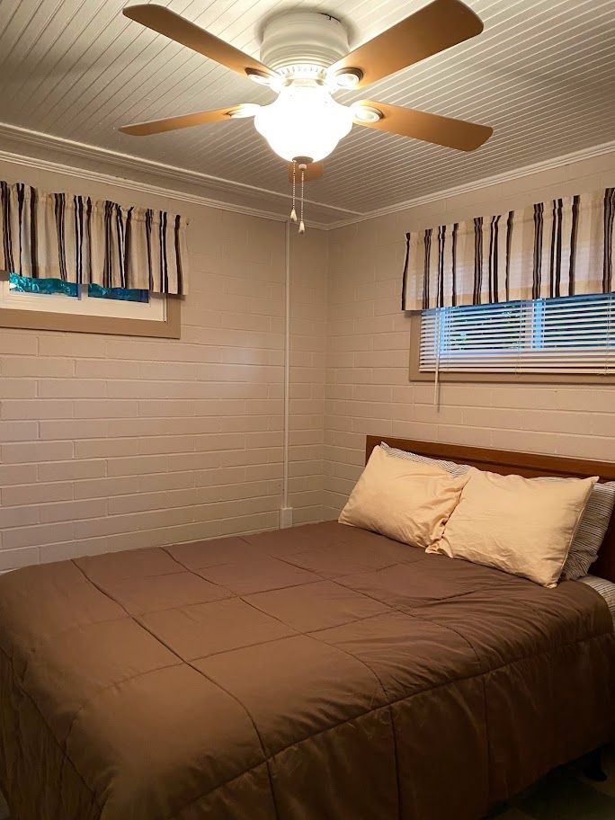 A bedroom with a bed , ceiling fan and window.